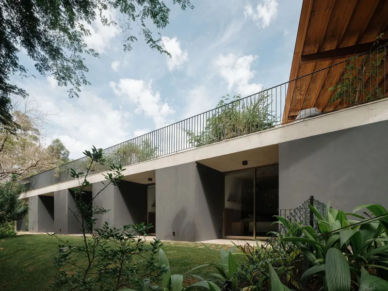 Concrete lower level facade with planted roof terrace balcony and steel railing under scattered clouds