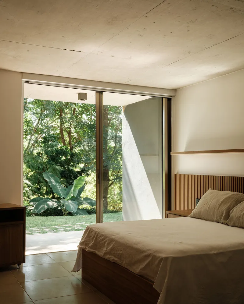 Bedroom with exposed concrete ceiling and sliding glass doors opening to garden with tropical plants