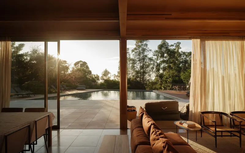 Living room with timber ceiling overhang framing view of lap pool and trees at sunset