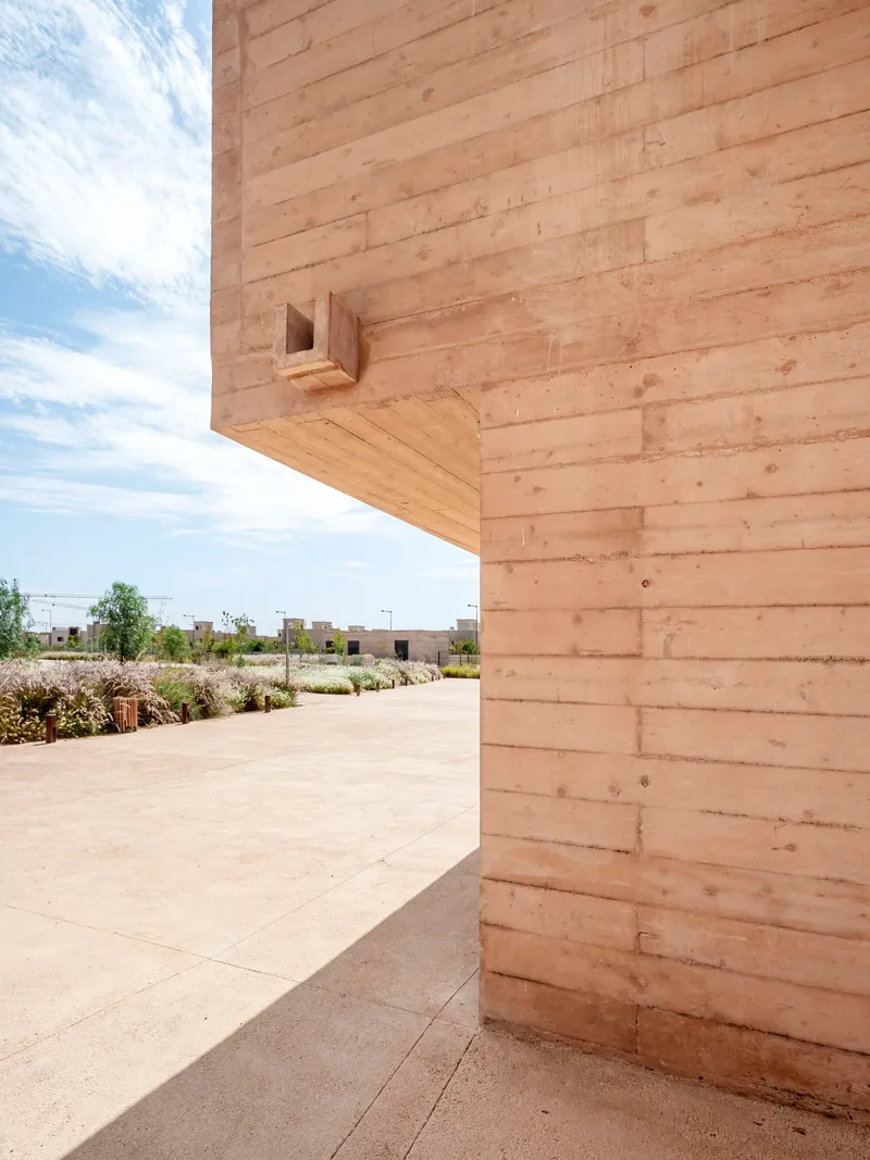 Corner detail of cantilevered rammed earth volume with small cubic birdhouse opening under clouds