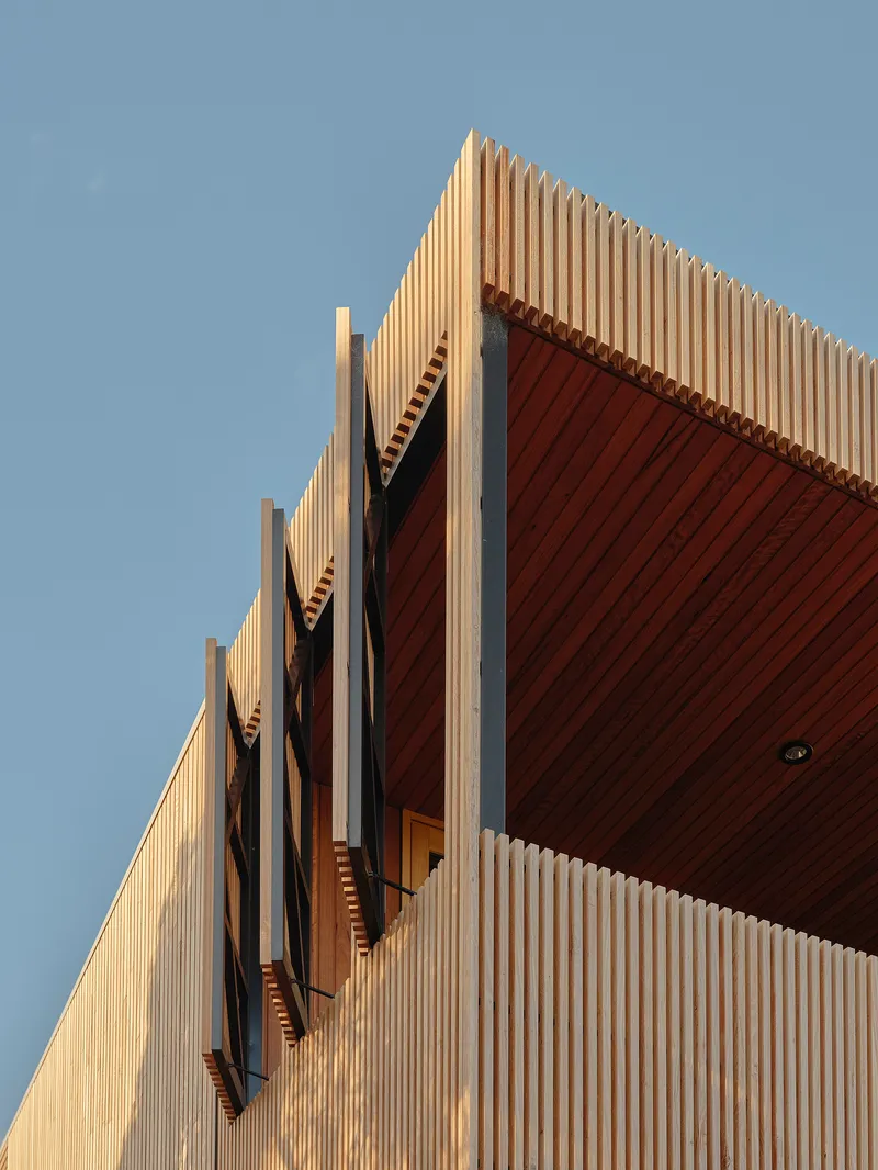 Upward view of vertical wood slat facade with recessed timber soffit against clear blue sky