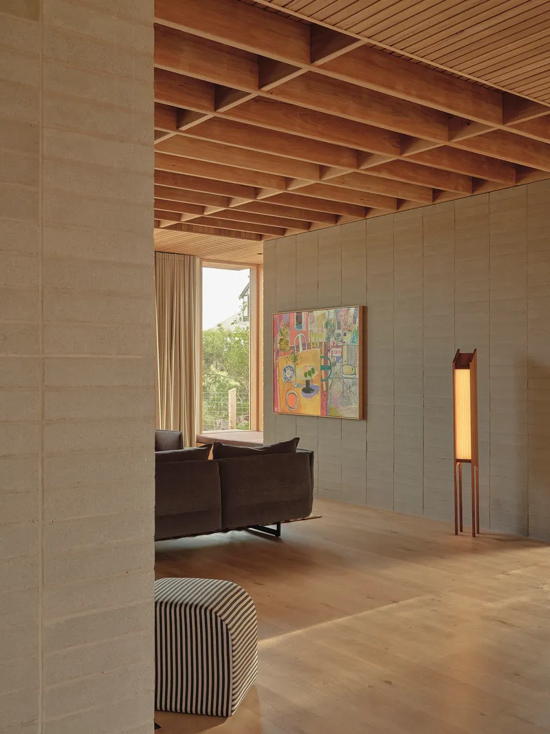 Interior living space with exposed timber beam ceiling and textured block wall opening to trees