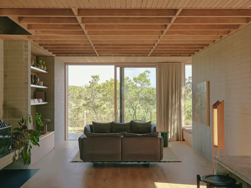 Living room framing floor-to-ceiling glazing that looks onto woodland with exposed timber joists above