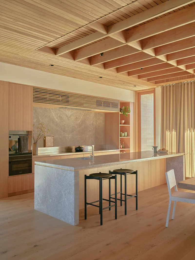 Kitchen island with stone base and timber joinery beneath exposed timber beams and slatted ceiling