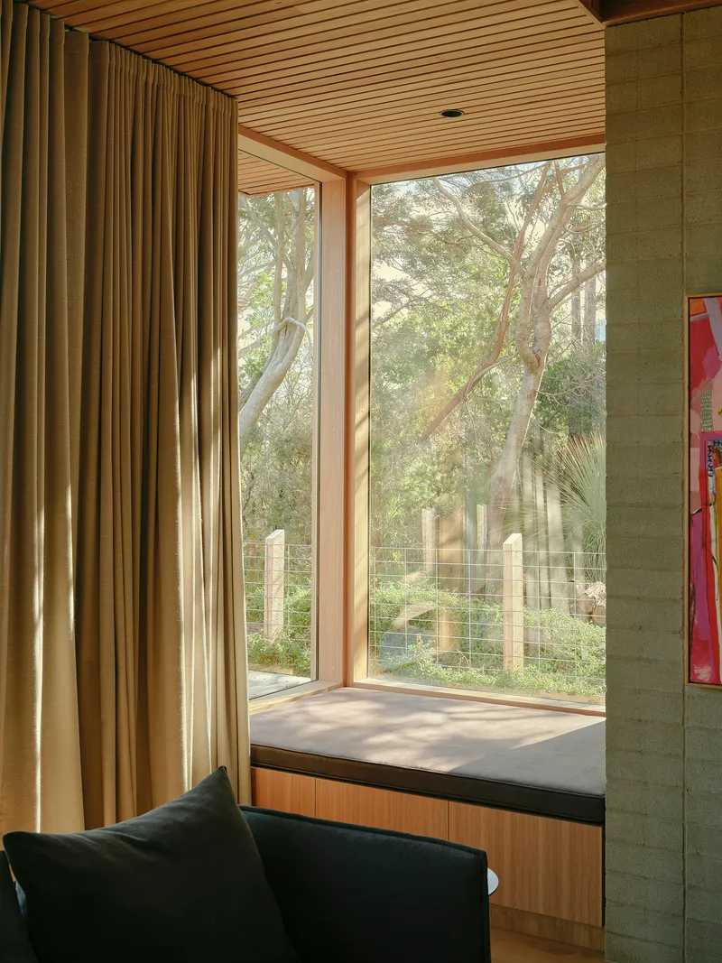 Window seat with timber frame and glazing overlooking garden trees in afternoon light