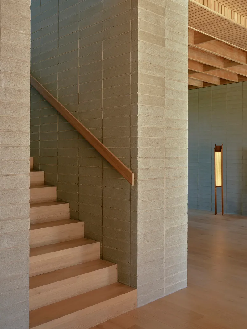 Timber stair with stone tile wall rising past exposed ceiling joists and floor lamp