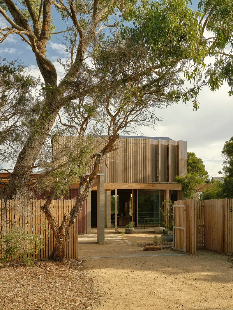 Two-storey timber screen facade with ground-level courtyard behind vertical slat fencing under overcast sky