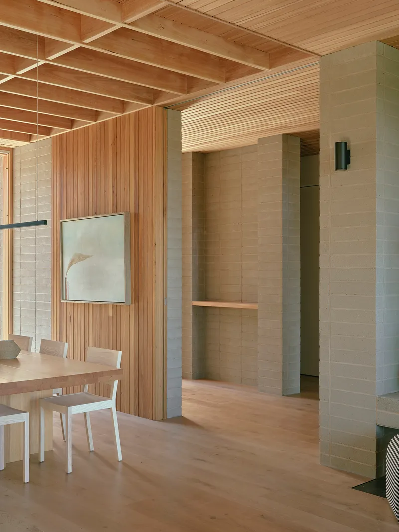Interior with exposed timber ceiling joists and rammed earth walls flanking a passage to dining area