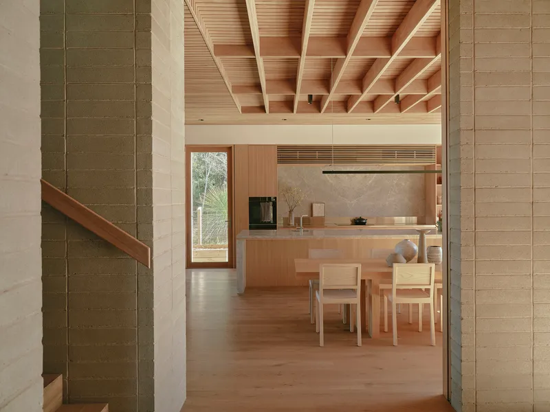 View through stone tile columns into kitchen and dining area with exposed timber ceiling structure