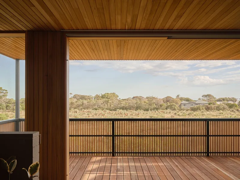 Timber deck with slatted balustrade overlooking native bushland under partly cloudy sky