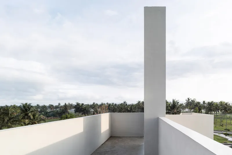 Rooftop terrace with tall square chimney rising above parapets and palm grove below