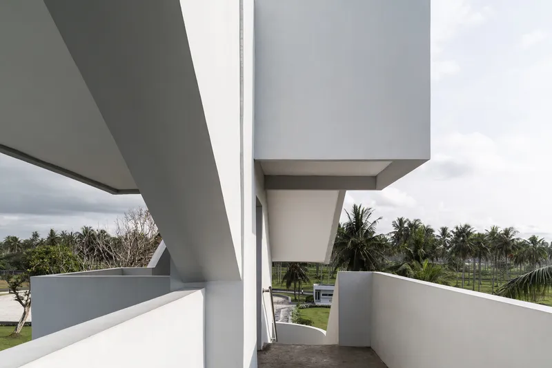 Upper-level outdoor passage with cantilevered slabs framing view of coconut palms and landscape
