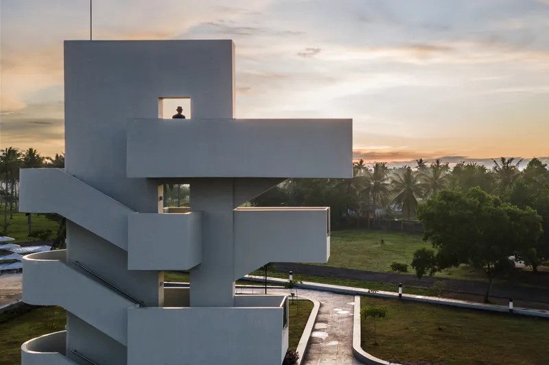 Stacked concrete viewing tower with cutout windows and exterior staircase at dusk