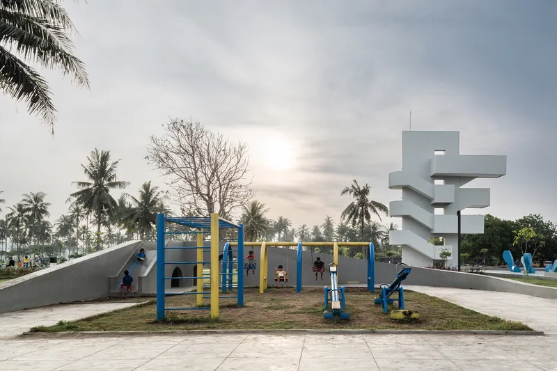 Children playing on blue and yellow playground equipment beside the white concrete tower at dusk