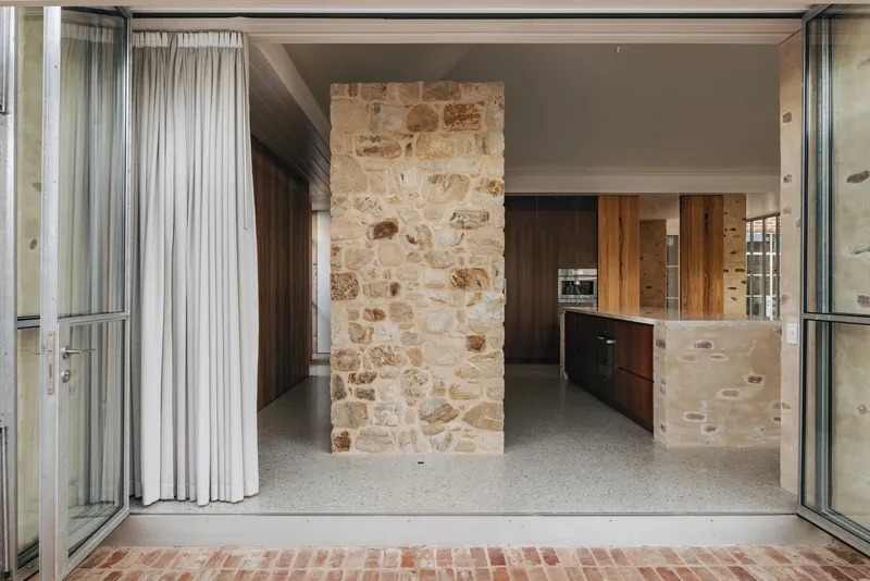 View through open glass doors to kitchen with freestanding sandstone wall and terrazzo flooring