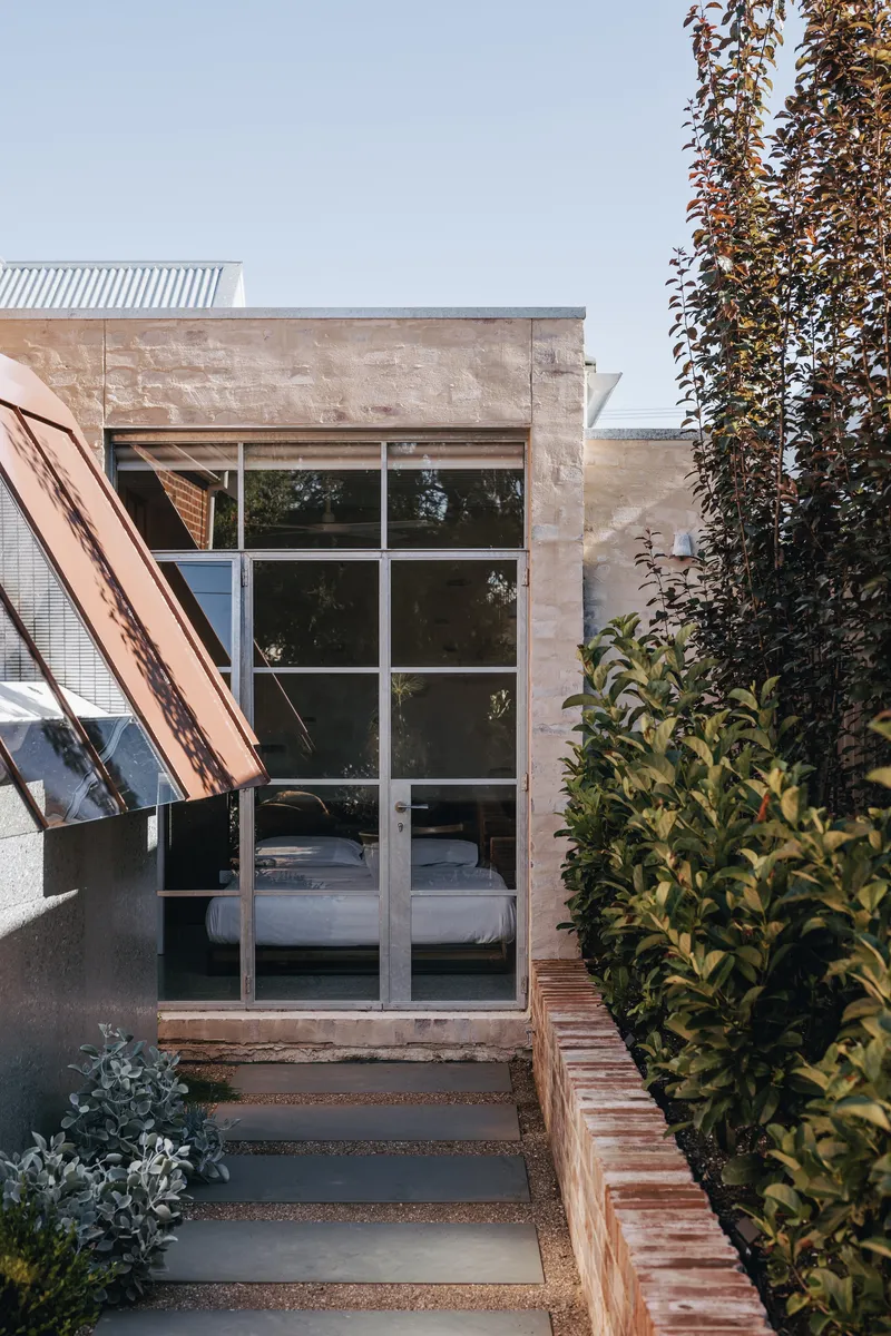 Exterior view of glazed doors leading to bedroom pavilion with sandstone walls and garden border