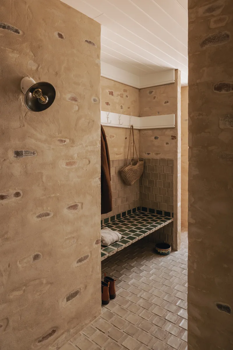 Entry alcove with stone walls, white timber ceiling and green tiled bench with hanging bag