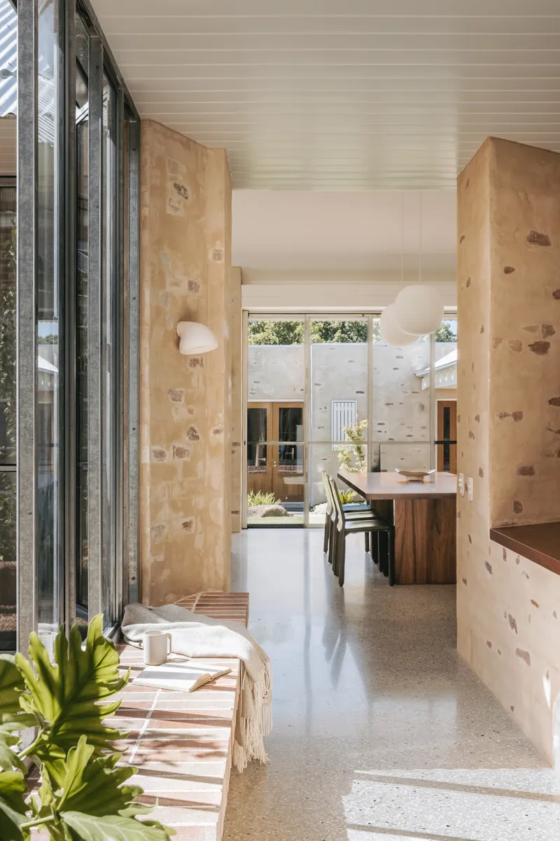 Open living space with stone walls, white ceiling panels and folding glass doors opening to courtyard