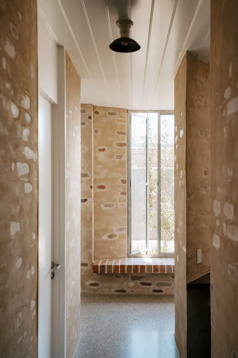 Narrow hallway with exposed stone walls leading to window seat in afternoon light