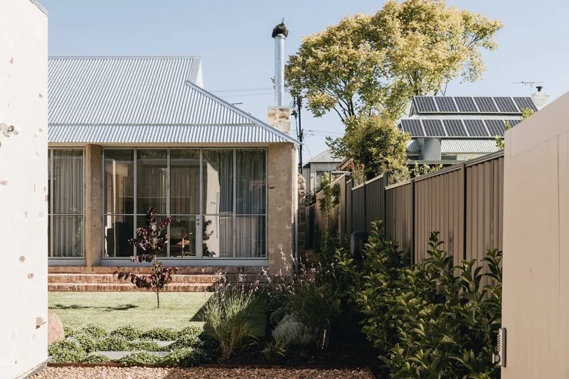Garden view showing corrugated metal cladding, stone walls and solar panels visible beyond planted beds