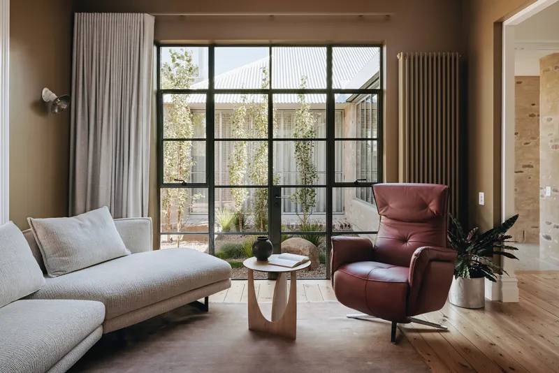 Interior sitting area with steel-framed glazed doors opening to a courtyard with climbing vines