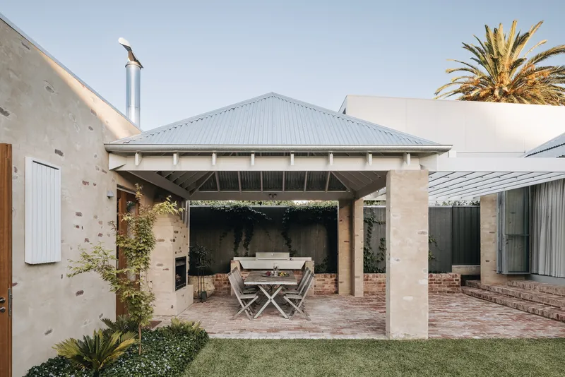 Covered outdoor terrace with stone columns and brick paving beneath a hipped metal roof