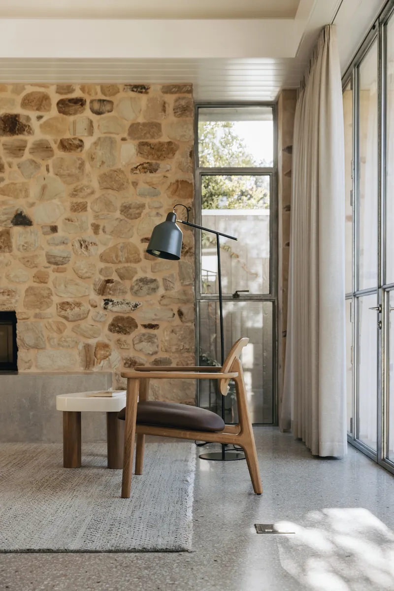 Reading corner with stone fireplace wall and steel-framed doors in morning sunlight