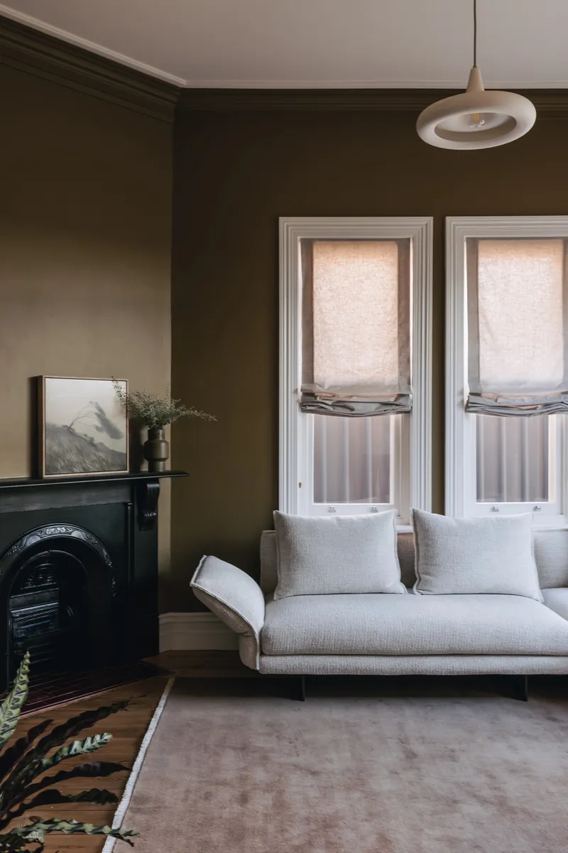 Living room with dark brown walls, a white sofa, black cast iron fireplace, and pendant light