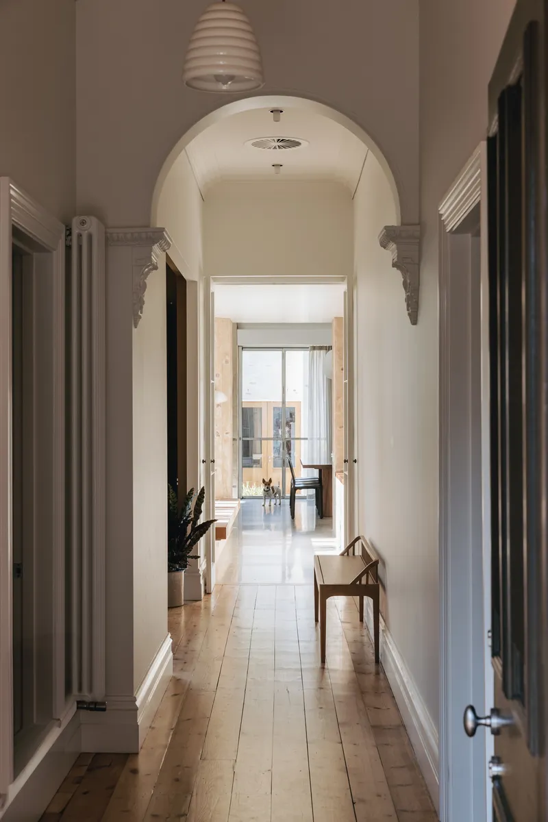 Arched hallway with timber floorboards leading to a sunlit room with french doors