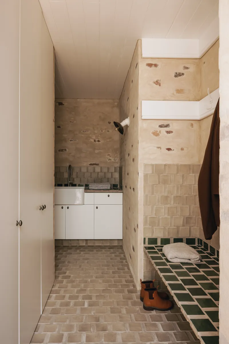Compact bathroom with exposed stone walls, beige tile floor, green tiled bench, and skylight above