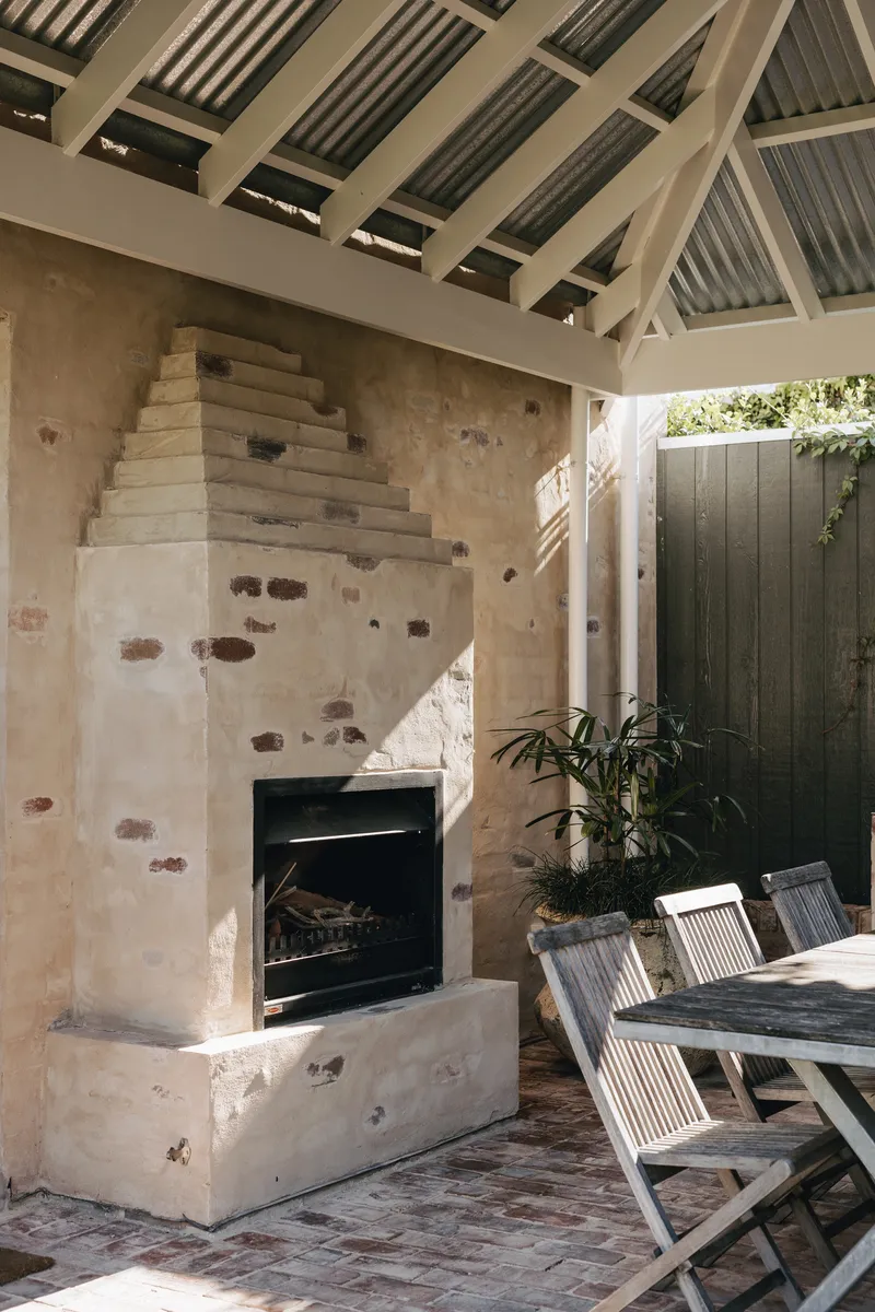 Stepped sandstone fireplace with exposed brick repairs under a painted timber rafter ceiling in afternoon light
