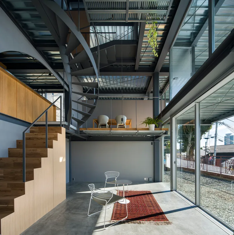 Triple-height interior with spiral staircase and stacked mezzanine platforms beneath a slatted ceiling open to sky