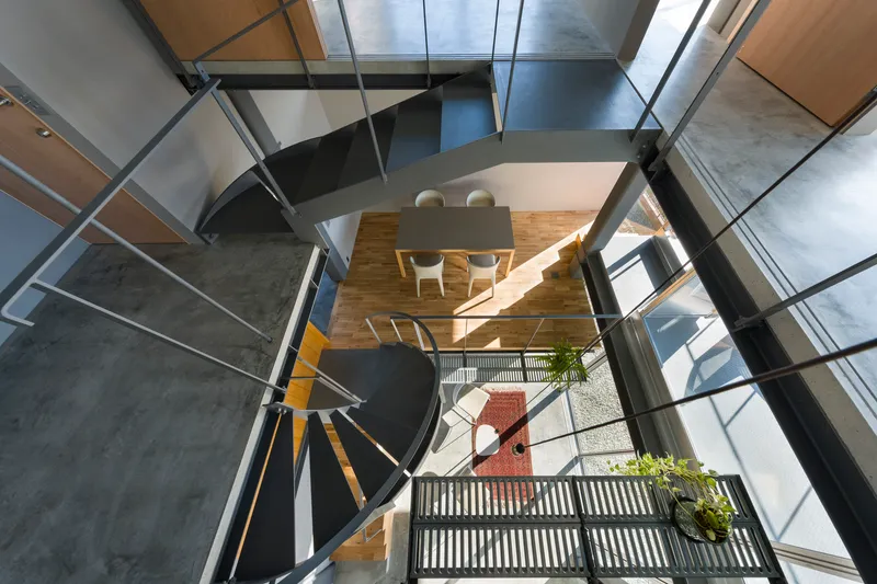 Top-down view through the spiral stairwell showing dining level and ground floor entry with glazed walls