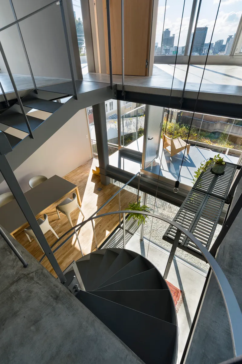 Looking down through the steel spiral staircase into the double-height space with terraced courtyard beyond