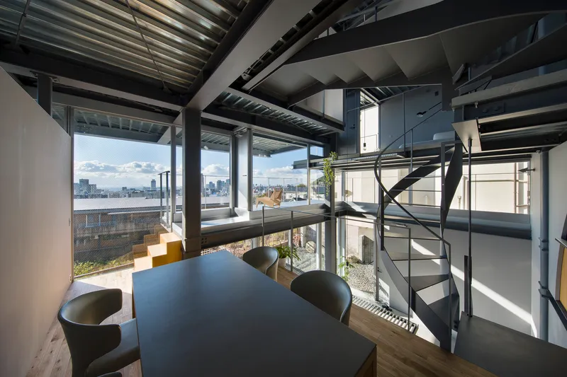 Open-plan dining area with exposed steel structure and spiral staircase overlooking the rooftop terrace