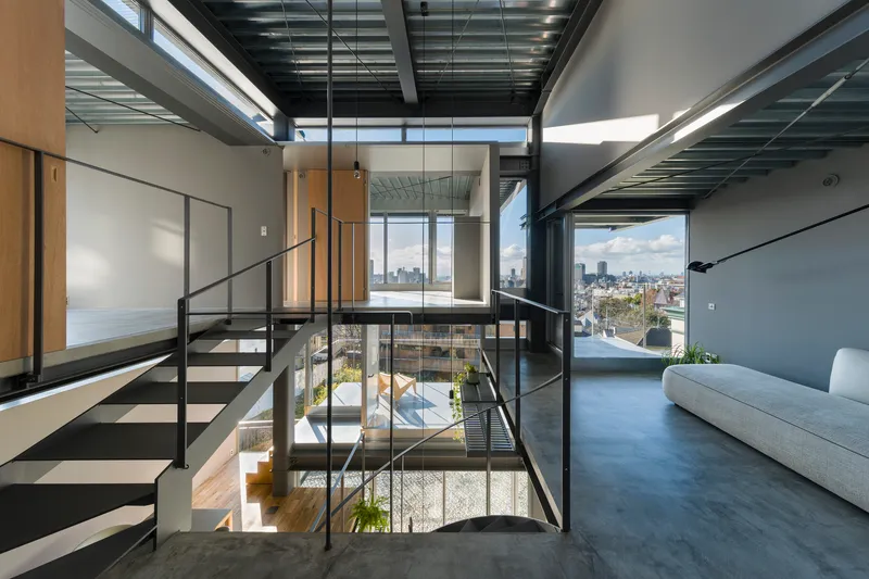 Steel staircase with mesh railings connecting multiple levels under a gridded skylight ceiling with city views