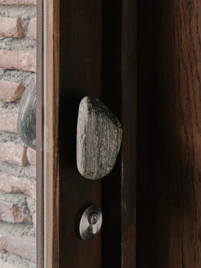 Weathered driftwood door handle mounted on timber door frame beside exposed brick wall