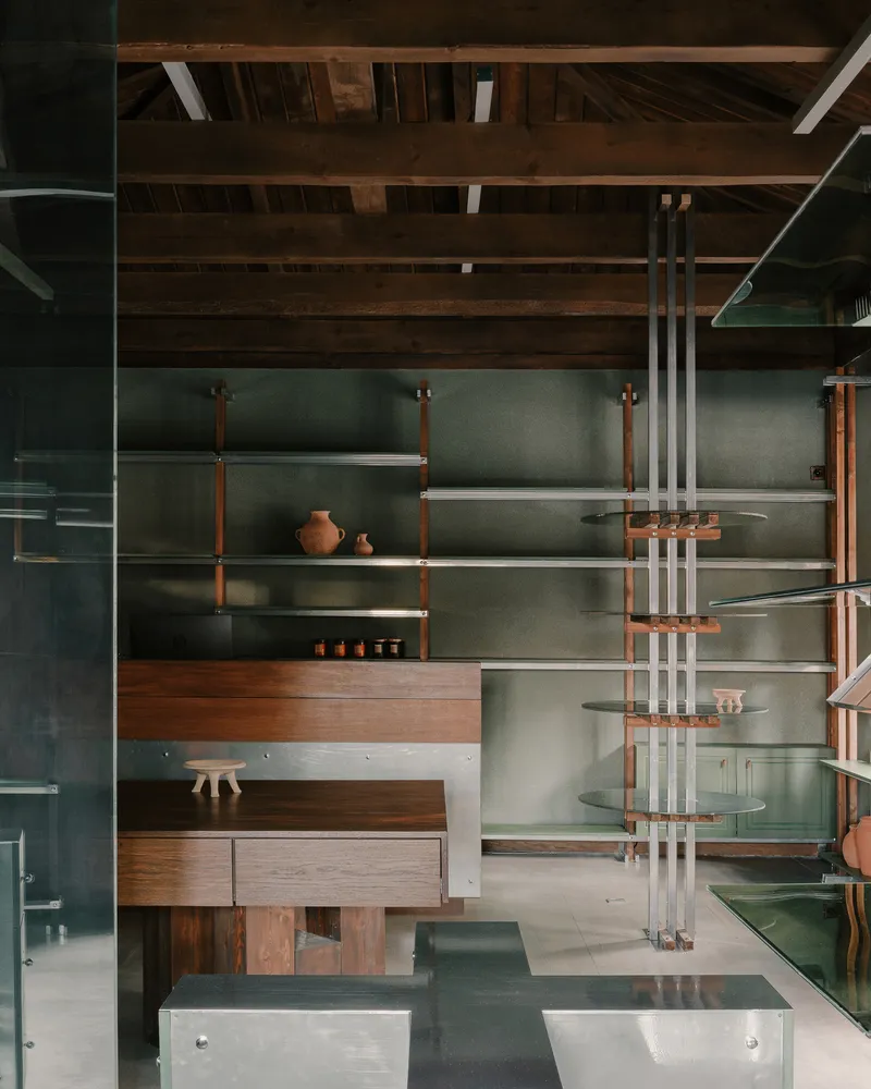 Detail of timber and metal shelving system with glass surfaces and ceramic vessels against a green painted wall