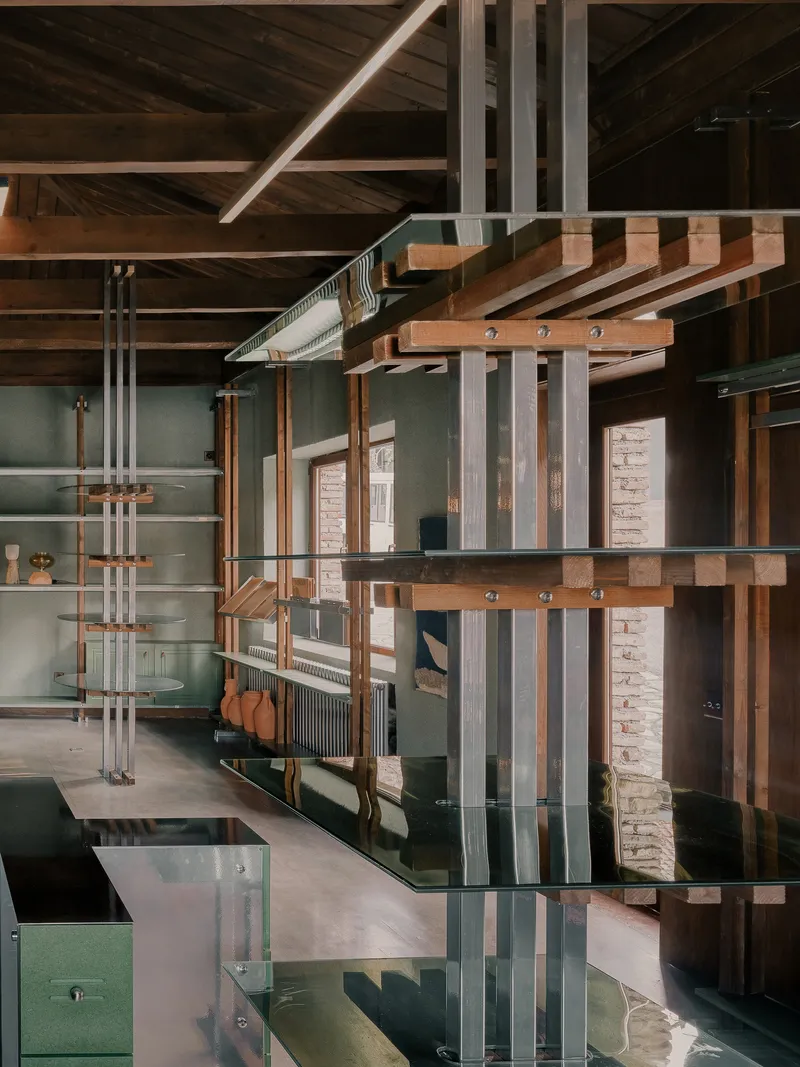 View through freestanding metal and timber shelving structure with glass surfaces reflecting the exposed roof beams above