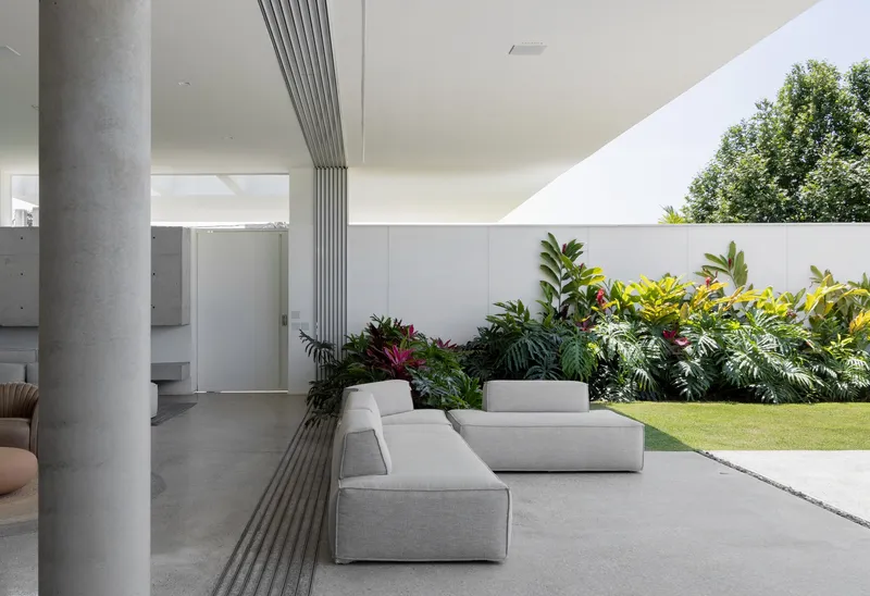 Outdoor seating area with grey lounge modules under a ribbed ceiling beam and lawn beyond