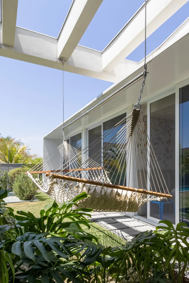 Rope hammock hanging beneath the white pergola beams with tropical plants framing the foreground