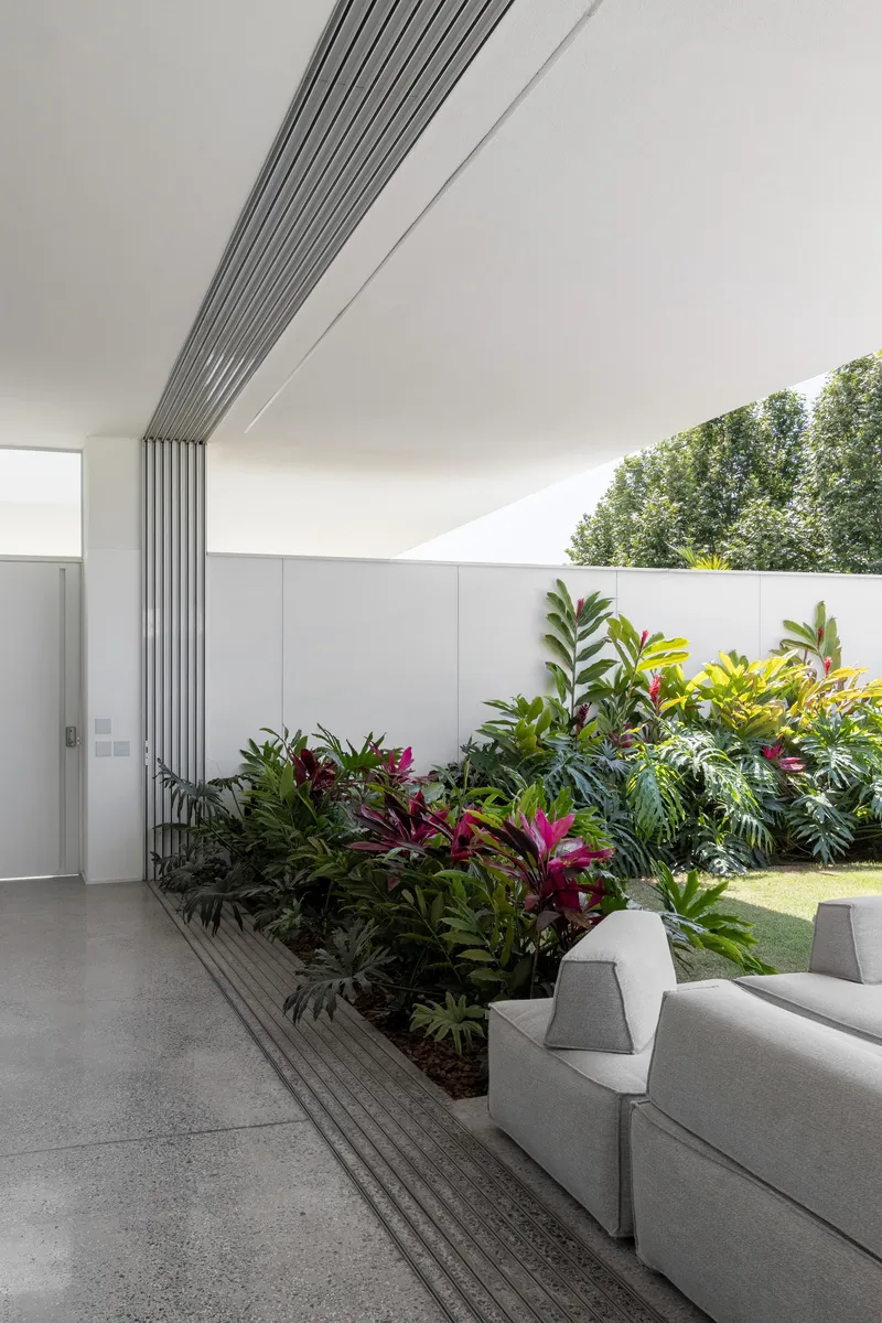 Interior courtyard with linear metal louvres meeting a planted bed of tropical foliage along the wall