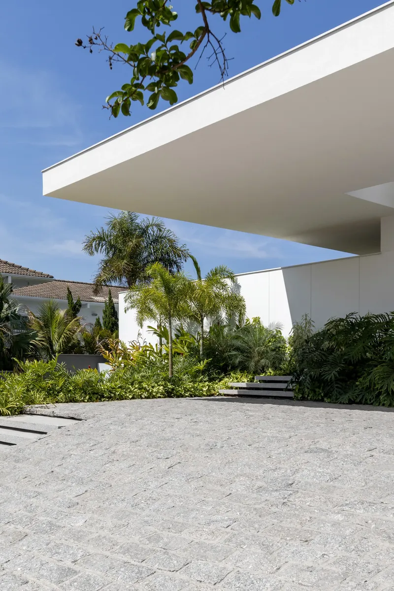 Entry courtyard with stone paving under cantilevered roof plane framed by palm trees and blue sky