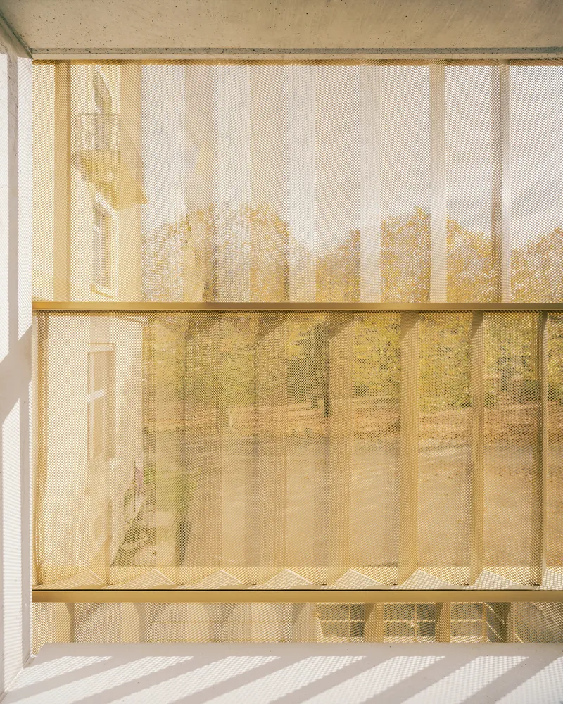 Close-up of bronze mesh facade with vertical slats filtering sunlight onto interior surfaces