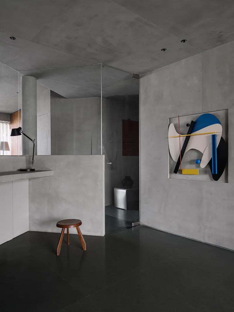Open living area with concrete walls, dark resin floor, and abstract artwork beside glass partition