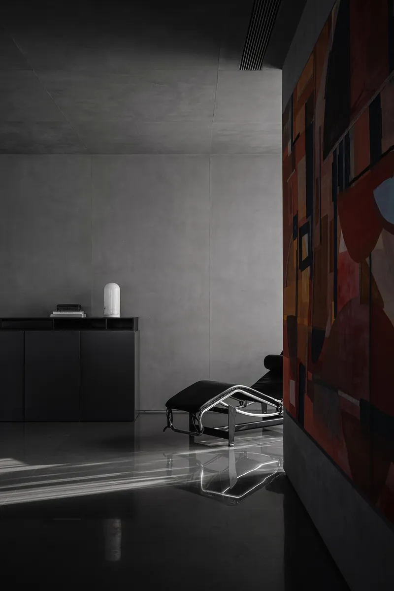 Interior corner with grey concrete walls and a low armchair beside a colorful abstract painting
