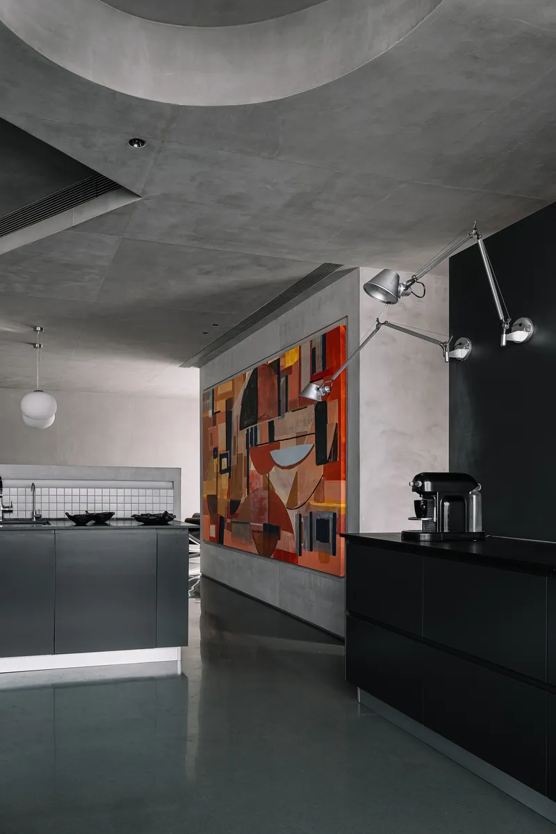 Kitchen area with black cabinetry and colorful geometric mural behind a grey concrete partition wall