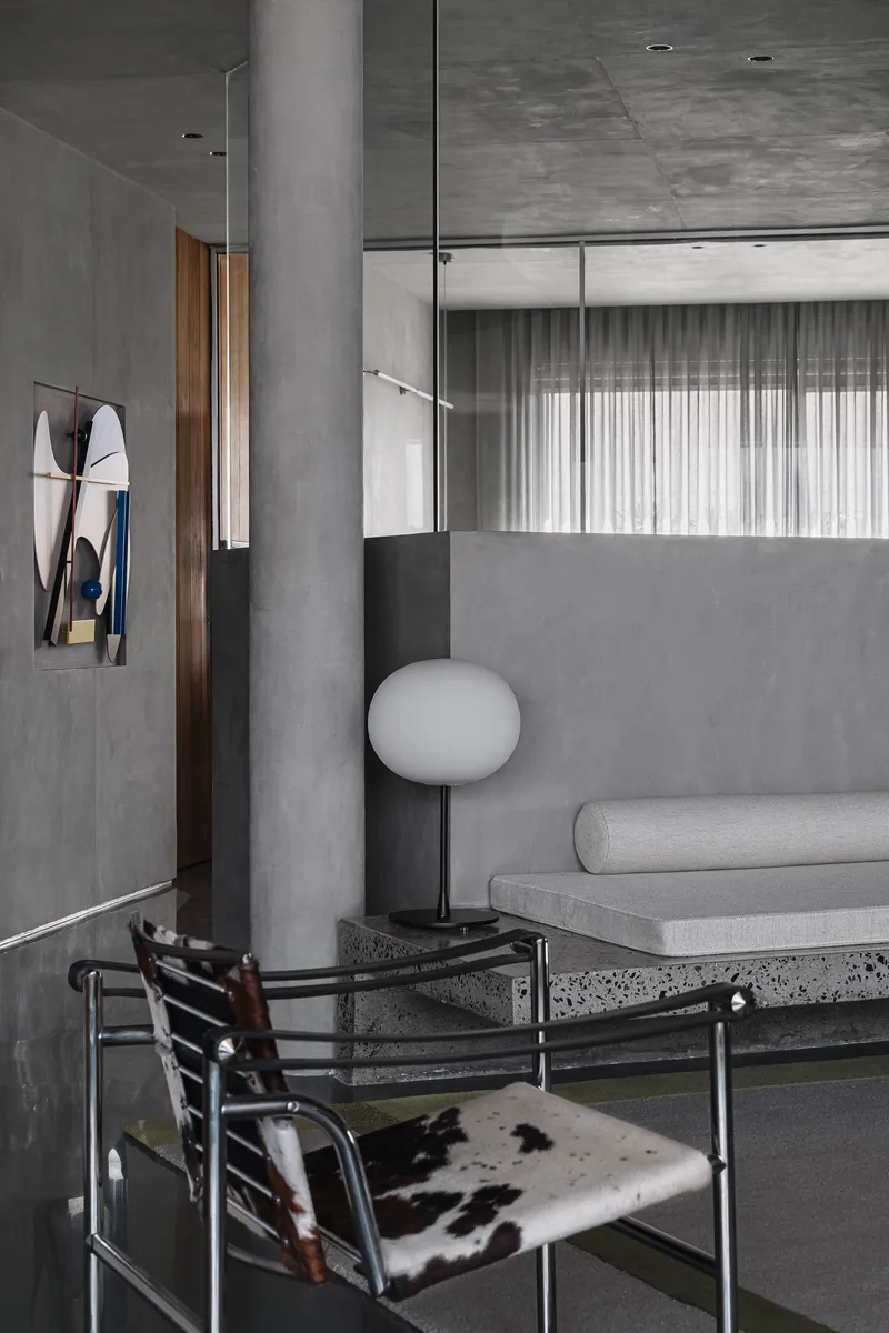 Seating nook with terrazzo bench, cowhide chair, and frosted glass partition overlooking sheer curtains
