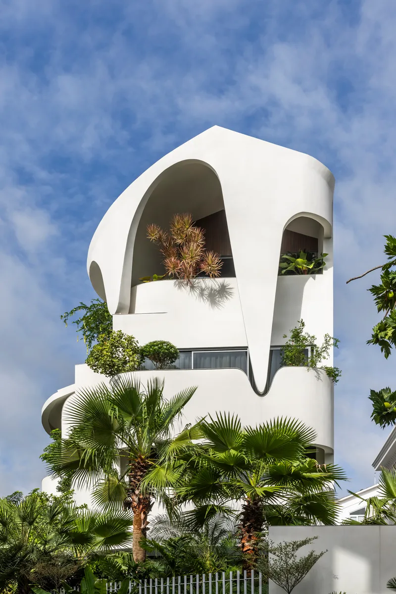 White facade with large arched openings framing potted pines against a clear blue sky
