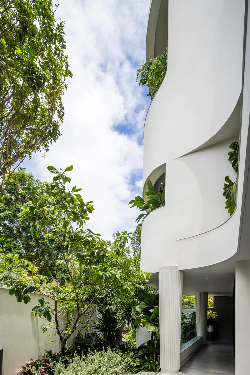 Upward view of spiraling white balconies with planted edges beside a deciduous tree